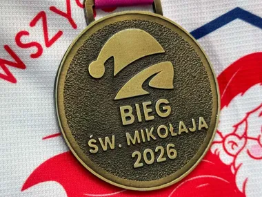 Medal z napisem „BIEG ŚW. MIKOŁAJA 2026” leży na tkaninie z motywem świątecznym.